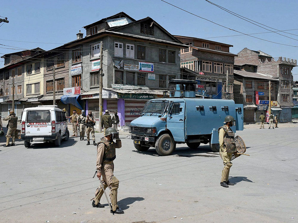 Police and CRPF personnel stand guard during restrictions imposed by the goverment authorties and strike call given by Hurriyat Confrence following the killing of a youth, in Batamaloo area of Srinagar on Sunday. PTI Photo