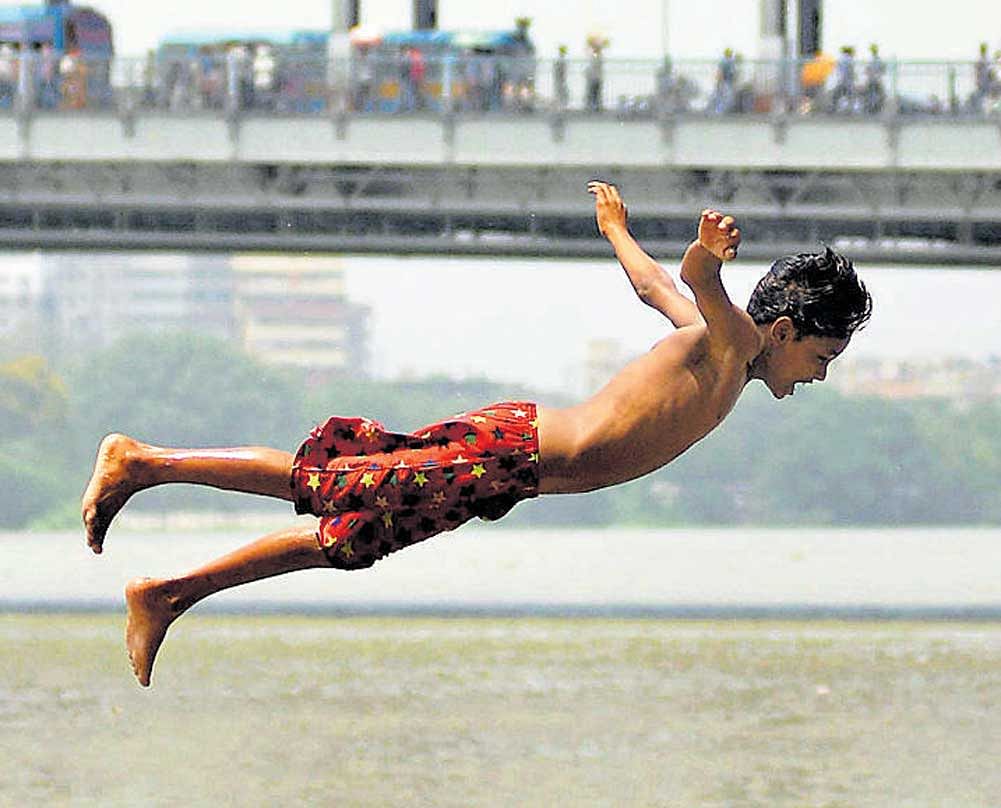 cooling off: A boy jumps into river Ganga in the backdrop of the Howrah Bridge in Kolkata. PTI photo