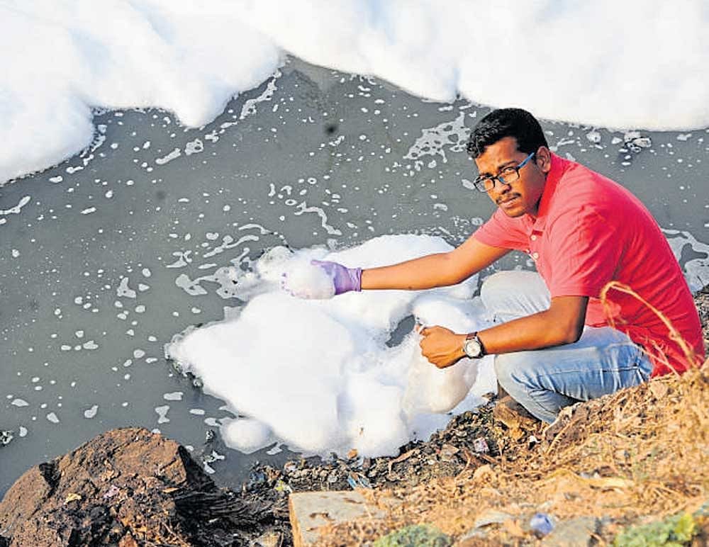 IISc student Vinay S takes a sample of foam from  Bellandur lake for study on Wednesday. DH photo