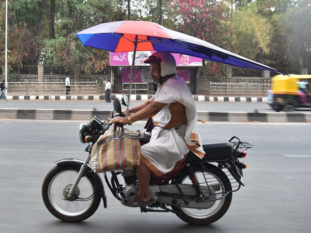 A two-wheeler rider uses an umbrella to escape from the rain on Palace Road in Bengaluru on Monday. DH Photo