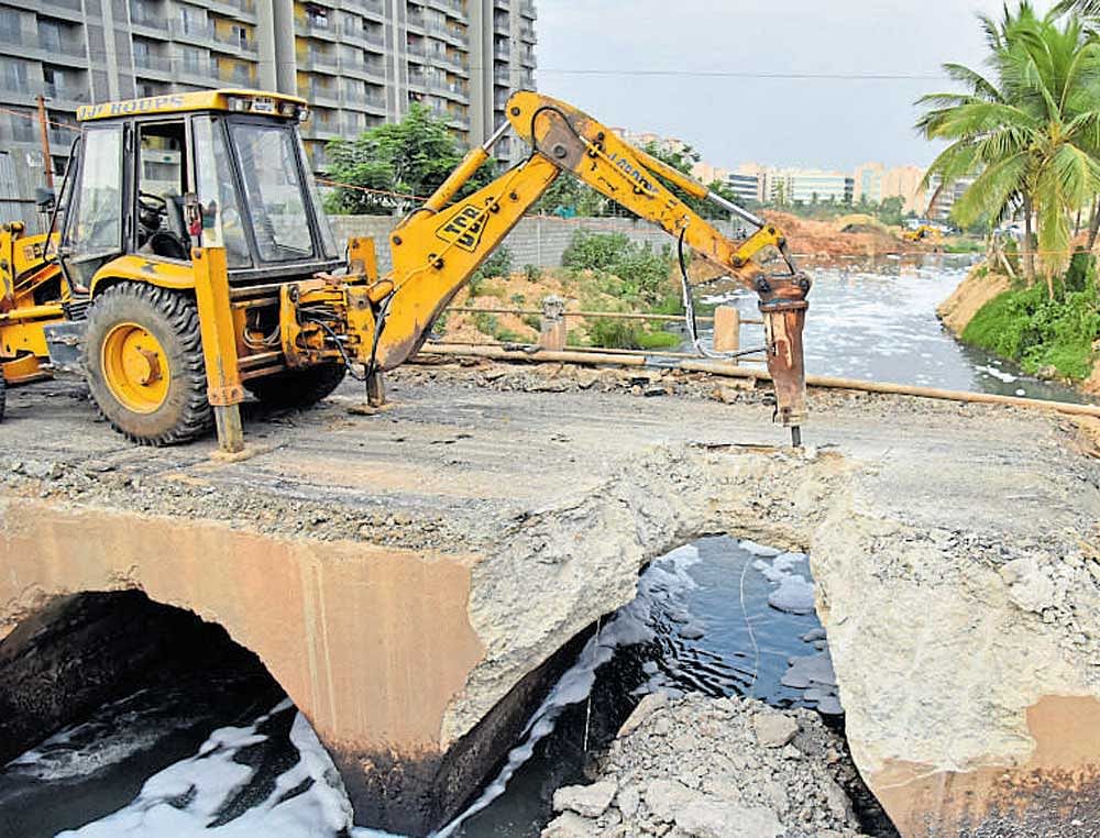 An earthmover demolishes an old bridge on Bellandur lake bund near Yemalur on Monday.  dh Photo