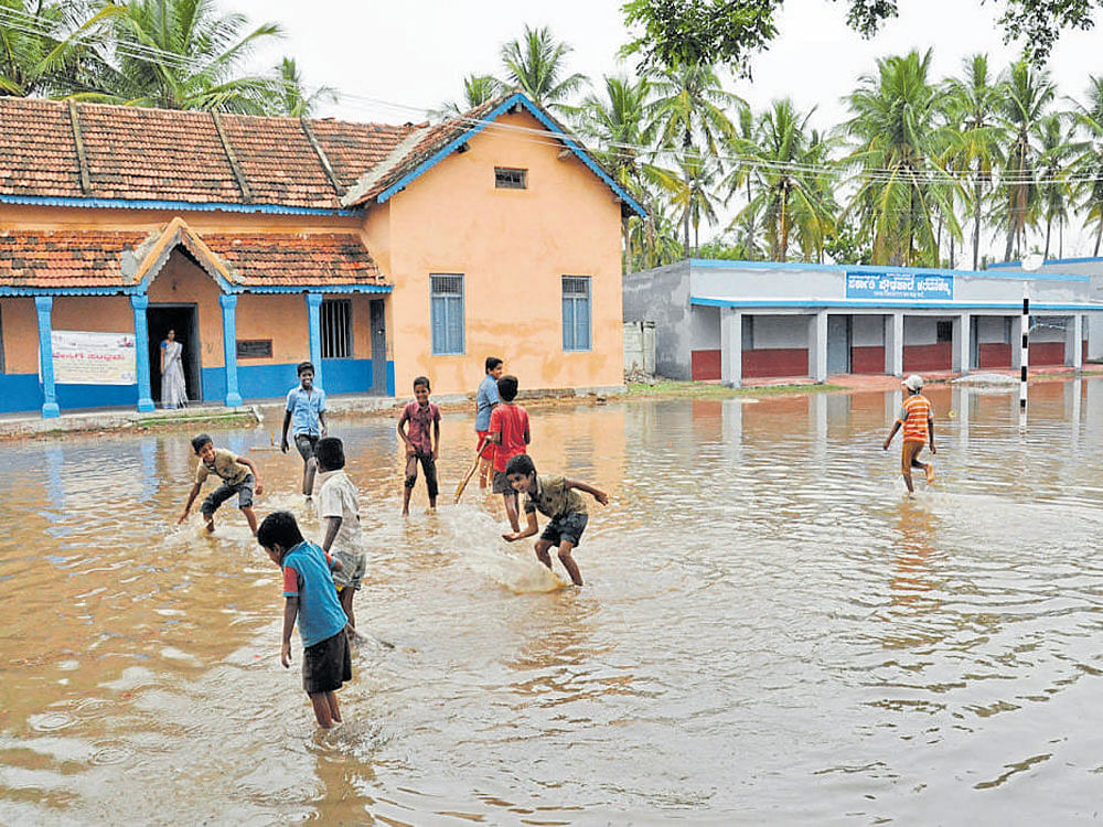 Schoolchildren play on the waterlogged premises of Haradanahalli Government High School in Chamarajanagar district on Thursday.