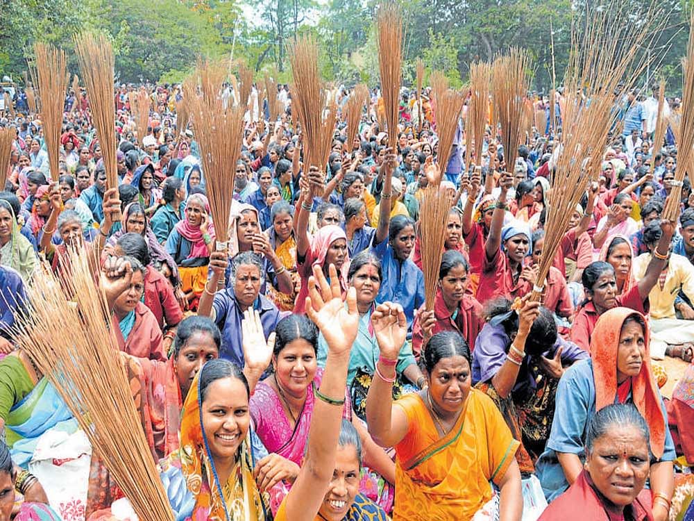 Contract municipal workers wield brooms as part of a protest rally at the Freedom Park on Thursday, demanding regular jobs and better pay. DH Photo