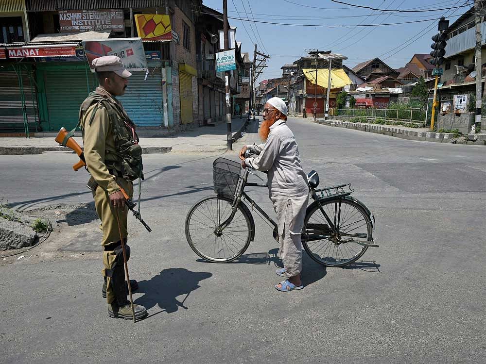 A security personnel stops a cyclist during curfew in Downtown Srinagar on Sunday. Authorities imposed curfew in the parts of Valley following the killing of a top militant commander at Tral in Pulwama District of South Kashmir Yesterday. PTI Photo