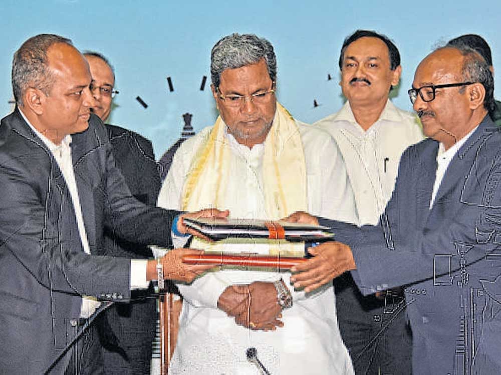 Siemens Industry Software India MD and CEO Suman Bose, and Government Tool Room & Training Centre Managing Director B N Gadag (R) exchange files after signing an MOU in the presence of Chief Minister Siddaramaiah in Bengaluru on Friday. DH Photo.