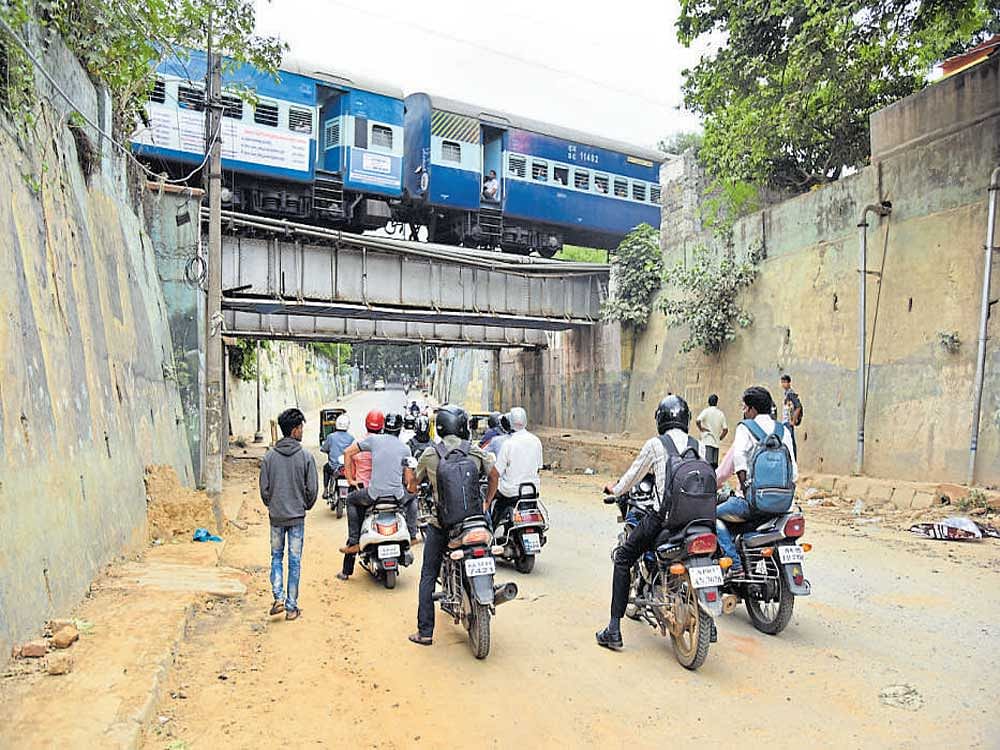 Two-wheeler riders wait ahead of the bridge near Kino theatre in Sheshadripuram as a train passes, fearing waste from the train  falling on them. DH Photo