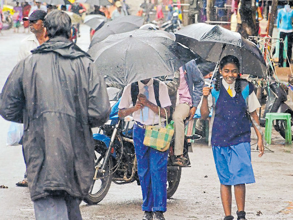 Students use umbrellas to protect themselves from rain in Belagavi on Tuesday. DH photo