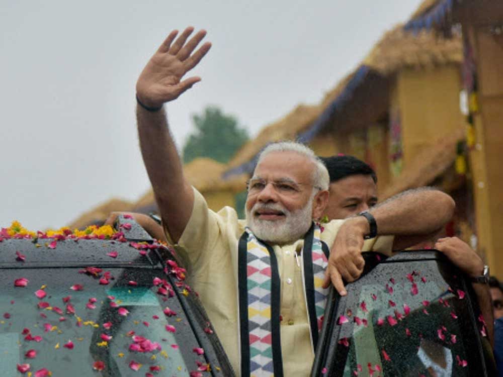 Prime Minister Narendra Modi waves at supporters during a road show in Rajkot, Gujarat on Thursday. PTI Photo