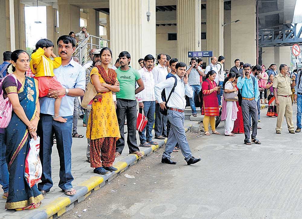 People wait for  BMTC  buses in front of the  Mysuru Road Metro  station on Friday.  DH Photo Srikanta Sharma R
