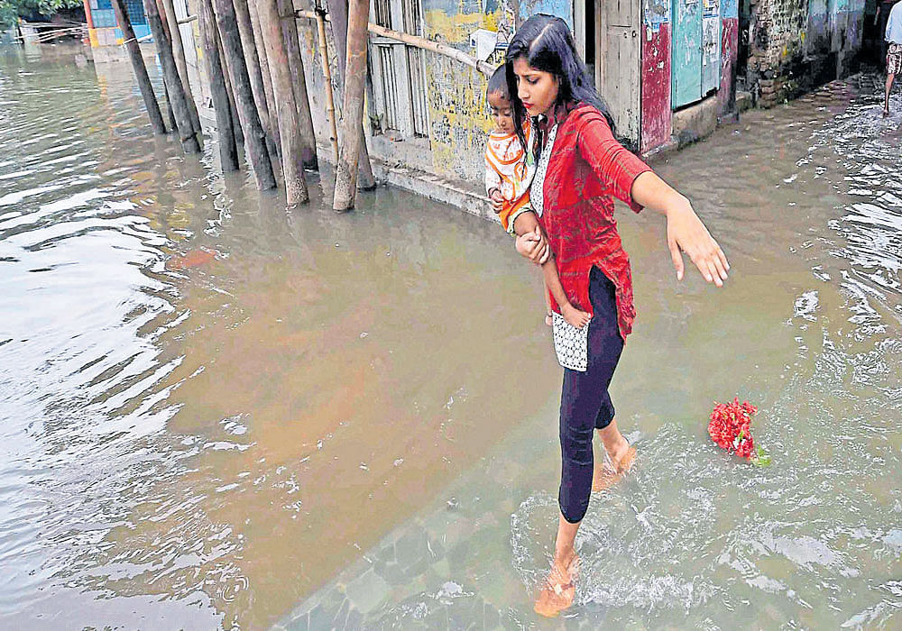 Knee-deep woes: A girl carries a child as she wades through a flooded street in Kolkata on Monday;  National Disaster Response Force men rescue a villager from a flood-hit area in Morbi district of Gujarat. PTI