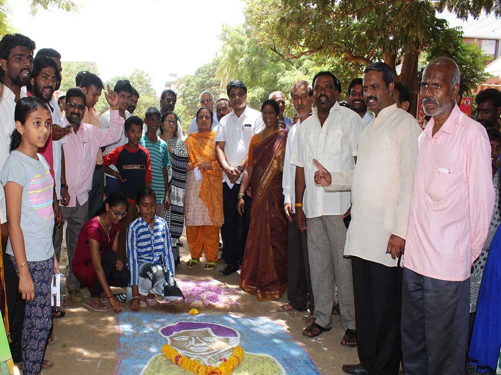 Residents of Shirur Park in Hubballi along with Physician Mahesh Nalvad admiring the 'Jagadish Shettar's' rongoli drawn by residents on the road as a means to protest against the bad roads in the City. DH Photo.