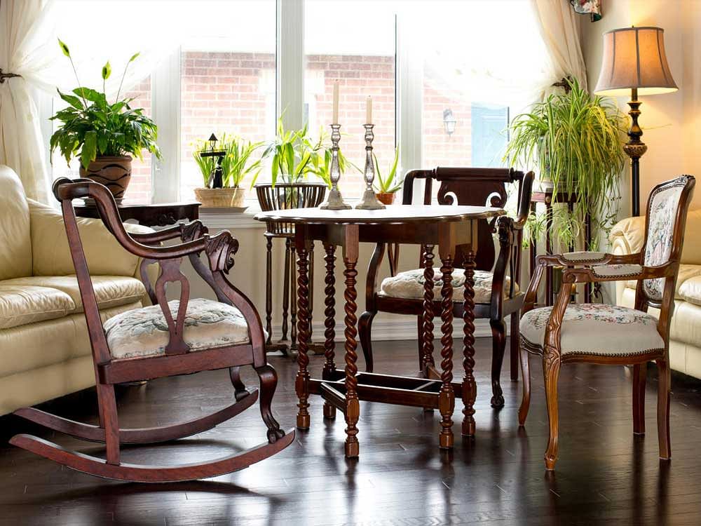 Against large windows facing the garden. Antique furniture (walnut table from 1930s, vintage chairs, side table, flower stand).interior design.