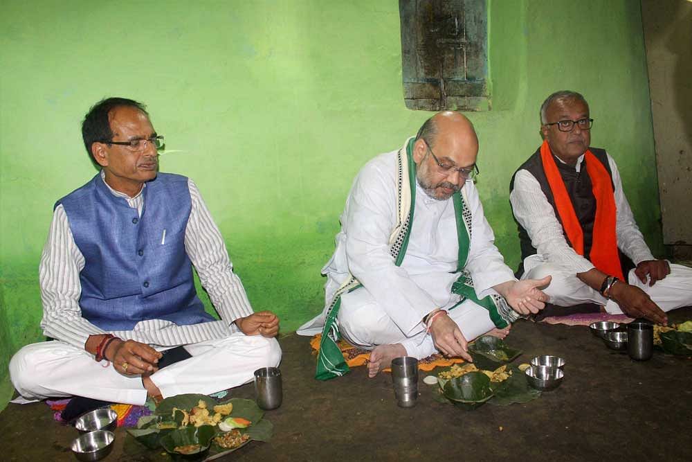 BJP National President Amit Shah with Madhya Pradesh Chief Minister Shivraj Singh Chouhan and BJP state president Nand Kumar Singh Chouhan having meals at the residence of the party worker Kamal Uike who belongs to Gond tribal community, in Bhopal. PTI photo.