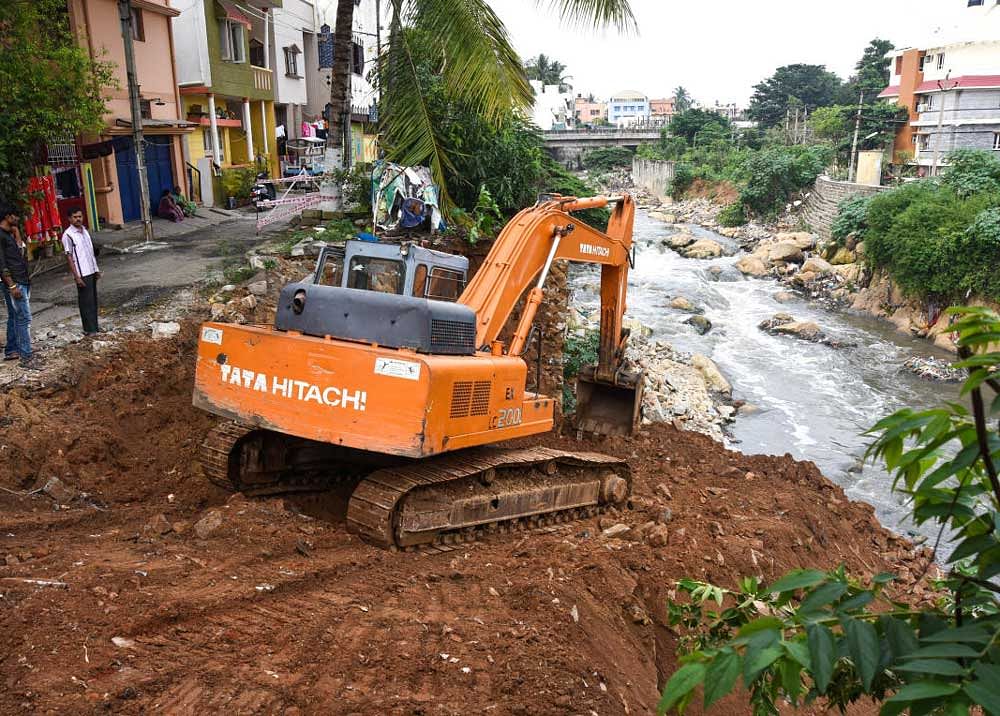 An excavator working on a the wall of a stormwater drain in Vijayanagar which had collapsed after incessant rain, on Monday. DH Photo
