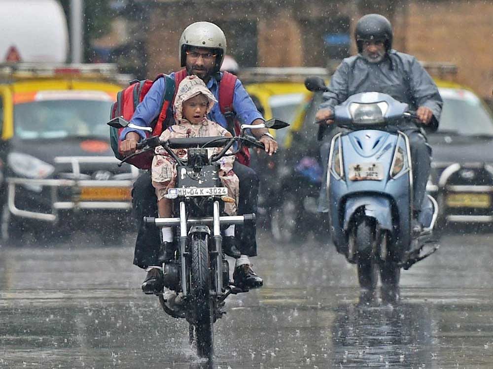 A man carries his child home from school on a motorcycle amid a downpour in Mumbai on Tuesday. PTI Photo