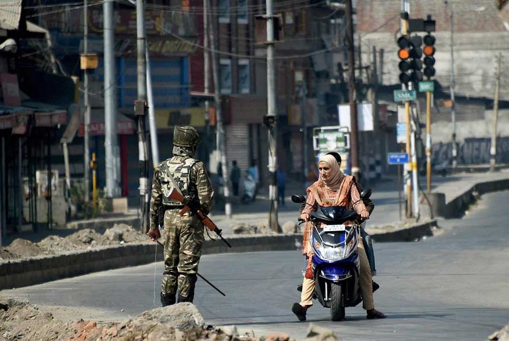 A security jawan stops a woman for identity check during restrictions in Srinagar on Monday. Authorities imposed curfew-like restrictions as a precautionary measures in downtown Srinagar as sepratist groups called for strike to protest against braid chopping in the Valley. PTI
