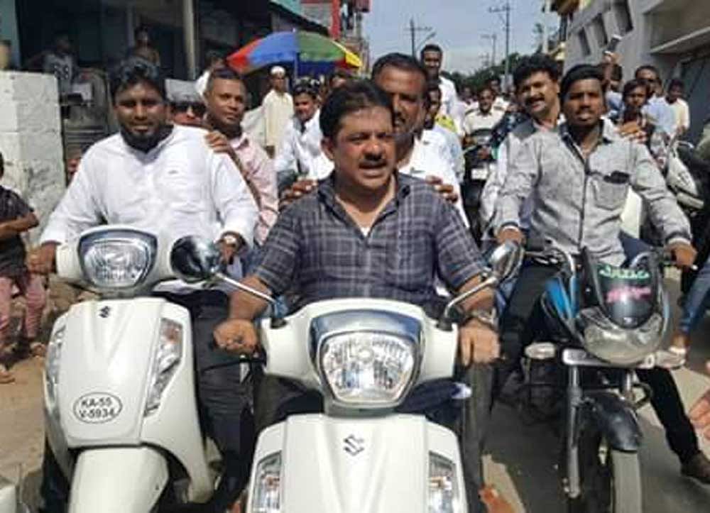 The Chamarajpet MLA is seen riding a scooter with a pillion, who is also not wearing a helmet. Image courtesy: Twitter