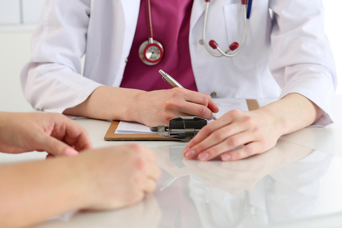 Female doctor hand hold silver pen filling patient history list at clipboard pad.