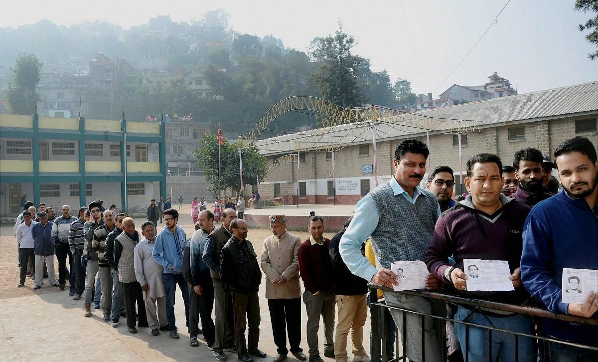 Voters in a queue show their voter identity card at a polling booth in Mandi, Himachal Pradesh on Thursday. PTI Photo