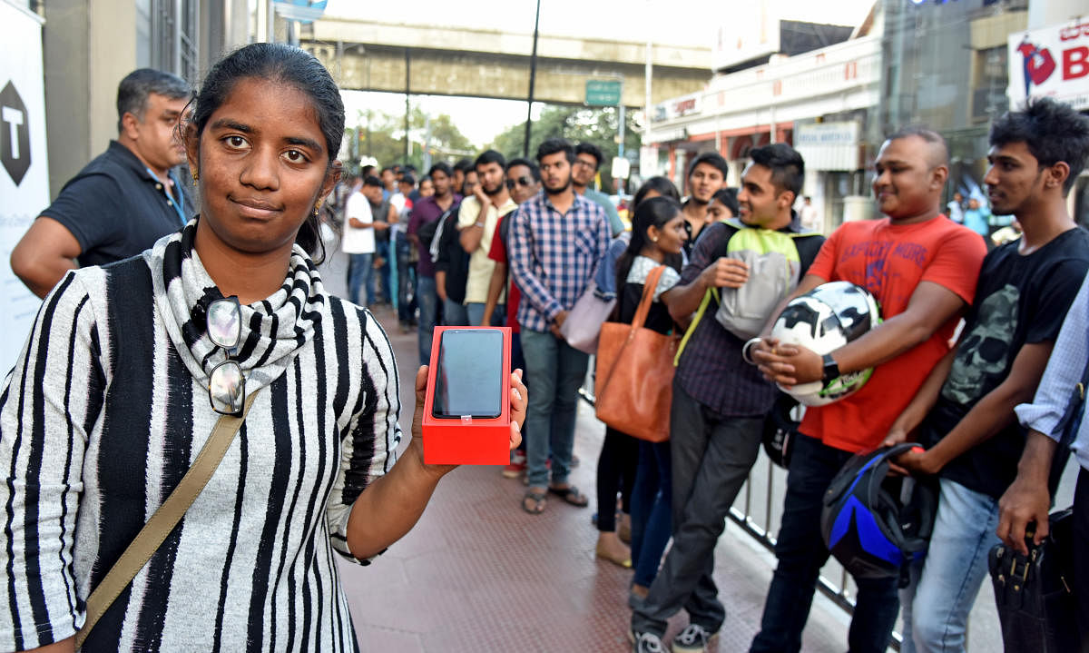 A Girl showing new One Plus 5T mobile phone, People standing in queue from Brigade road to MG Road Metro station to purchase One Plus 5T mobile phone in Bengaluru on Tuesday. Photo by S K Dinesh