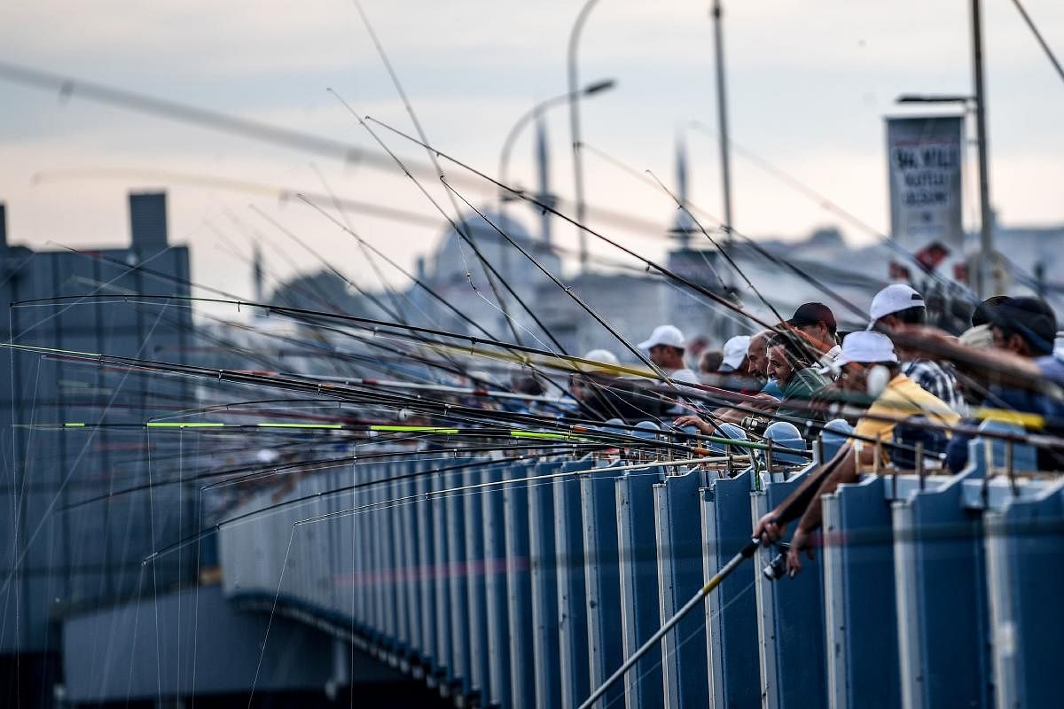 (FILES) This file photo taken on October 23, 2017 shows people fishing from the Galata Bridge in Karakoy district in Istanbul, as the new mosque is seen in the background. Experts have expressed concern over the decrease of fish in the Bosphorus river. / AFP PHOTO / OZAN KOSE