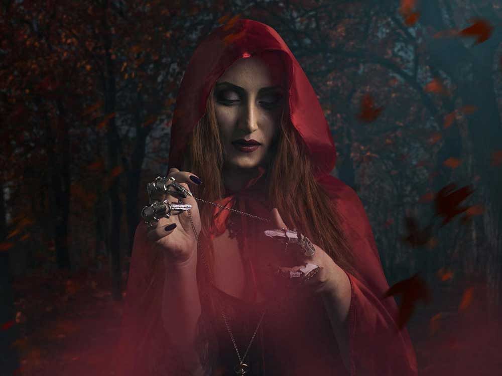 Beautiful sexy sorceress in red cloak holding antique clock watch standing in the forest photo.