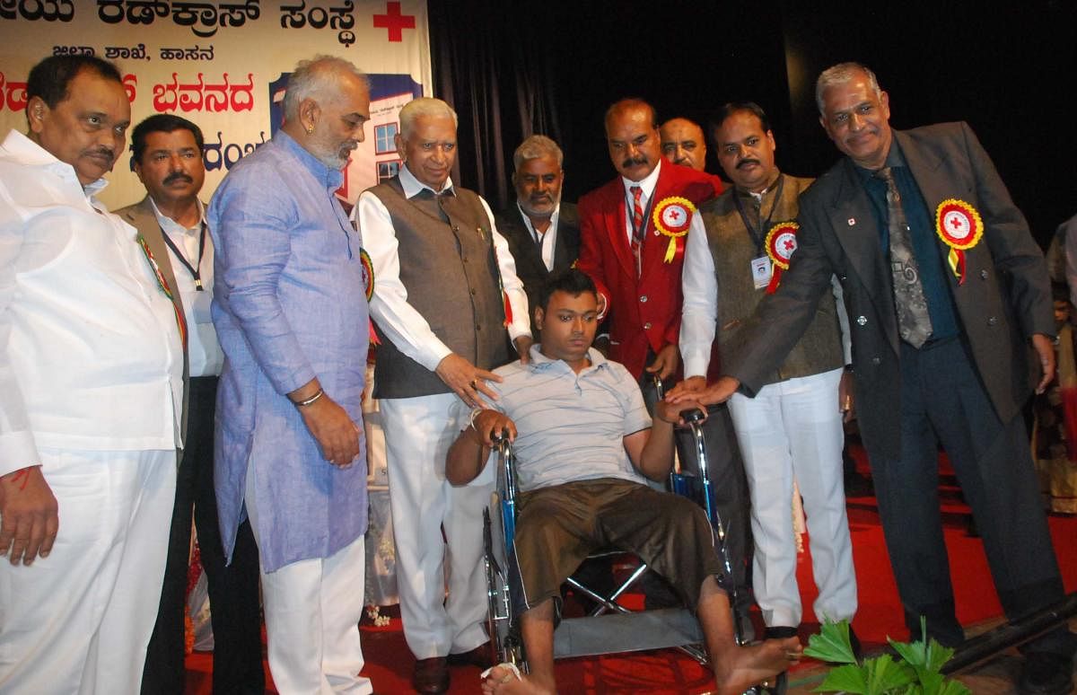 Governor Vajubhai Vala hands over a wheelchair to a physically challenged person during the inauguration of Red Cross Bhavan in Hassan on Thursday. District in-charge Minister A Manju is seen.