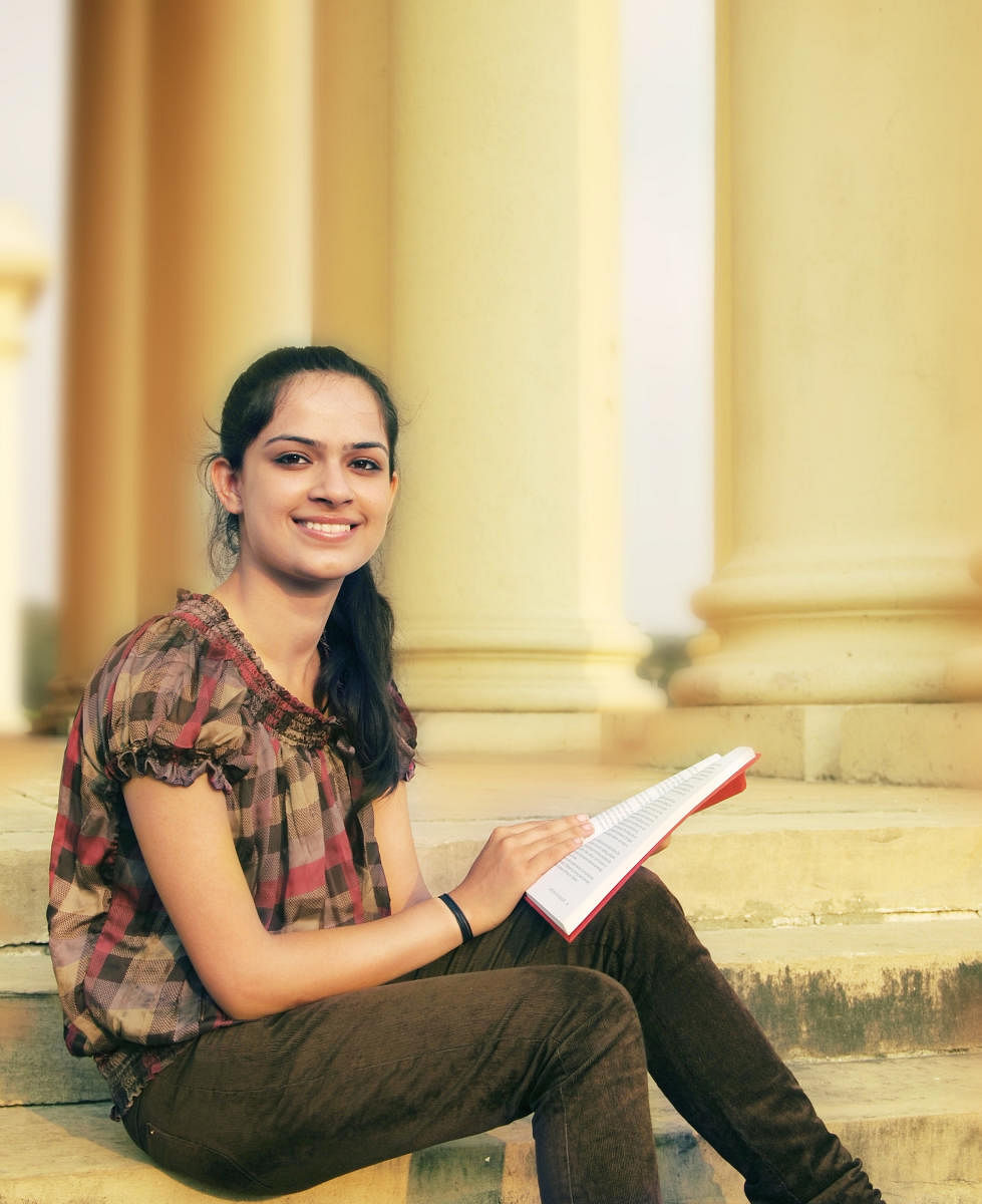 Cheerful female student sitting outdoor and reading book.