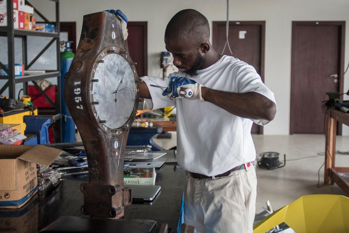 Ghanaian artist Joseph Awuah-Darko works on a clock, the pieces of which were found at Agbogloshie dumpsite, at his workshop at Ashesi University College where he studies, outside Accra on November 29, 2017. Joseph is the founder of Agbogblo.Shine Initiative, an organisation that advocates the use of design thinking to galvanize social change in Agbogbloshie to stop climate change. With the project, he also seeks to repurpose e-waste and scrap to create upcycled furniture. / AFP PHOTO / CRISTINA ALDEHUELA