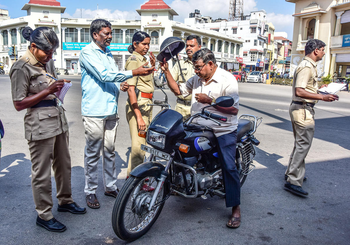 Police personnel check for ISI mark on helmets, at Nehru Circle in Mysuru on Tuesday. dh photo
