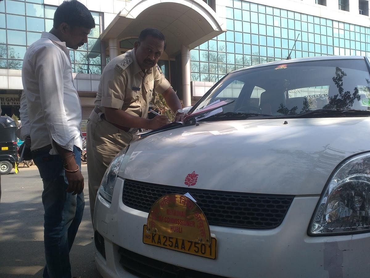 RTO personnel issue notice to the driver of a car hired by the government agency, during the drive against defective number plates, in Hubballi on Thursday.