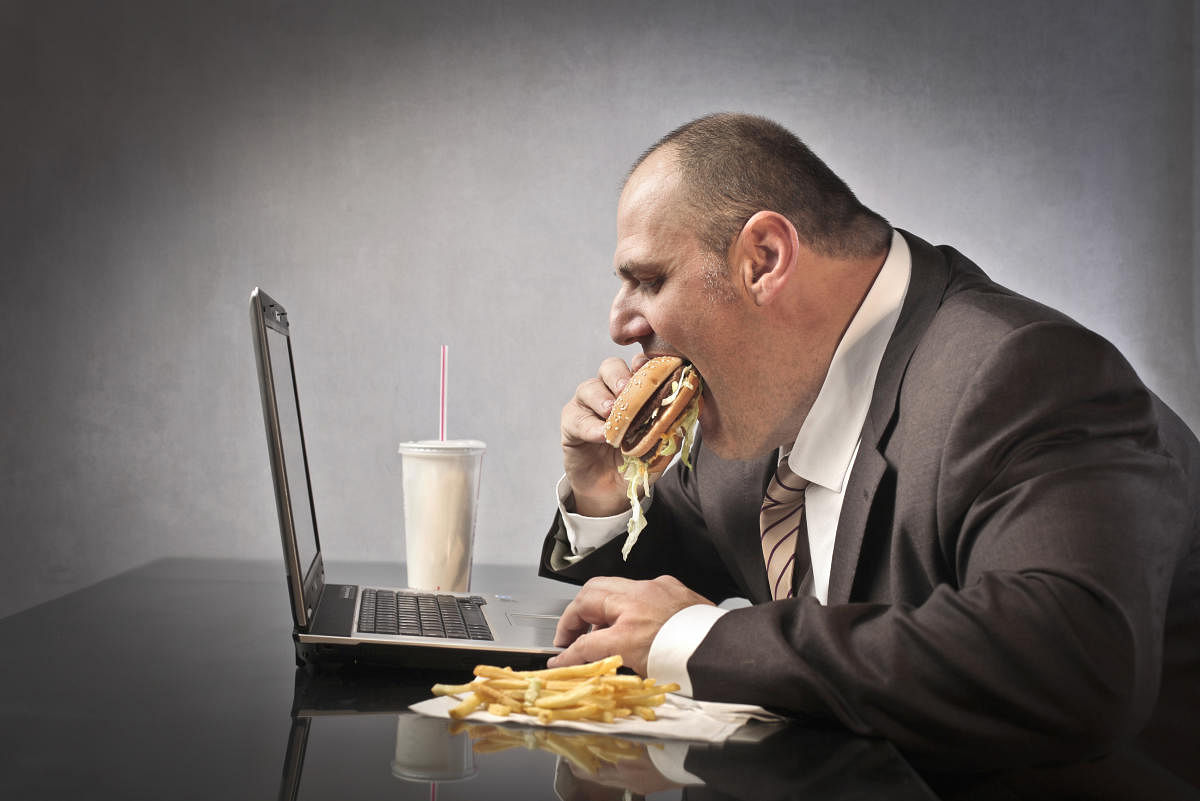 Fat businessman eating junk food in front of a laptop.