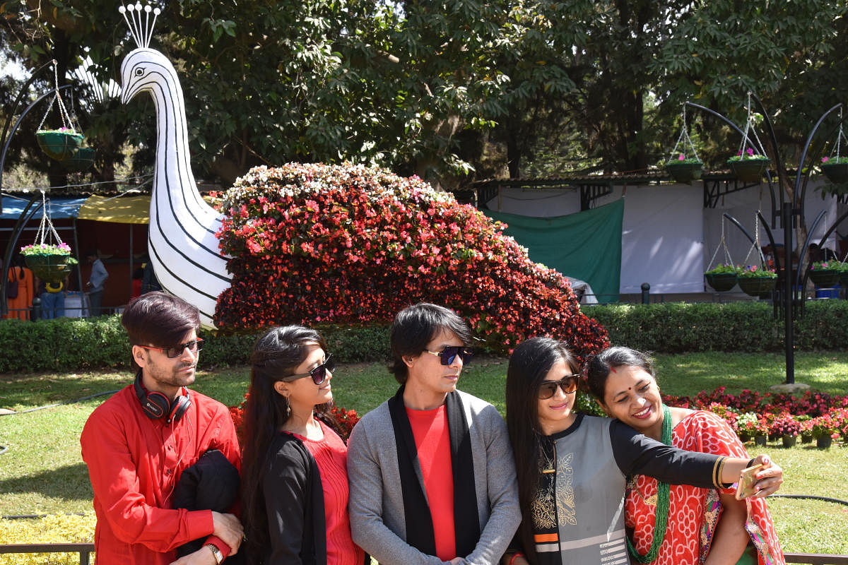 Visitors pose for a selfie in front of a floral structure. DH Photo by S K Dinesh