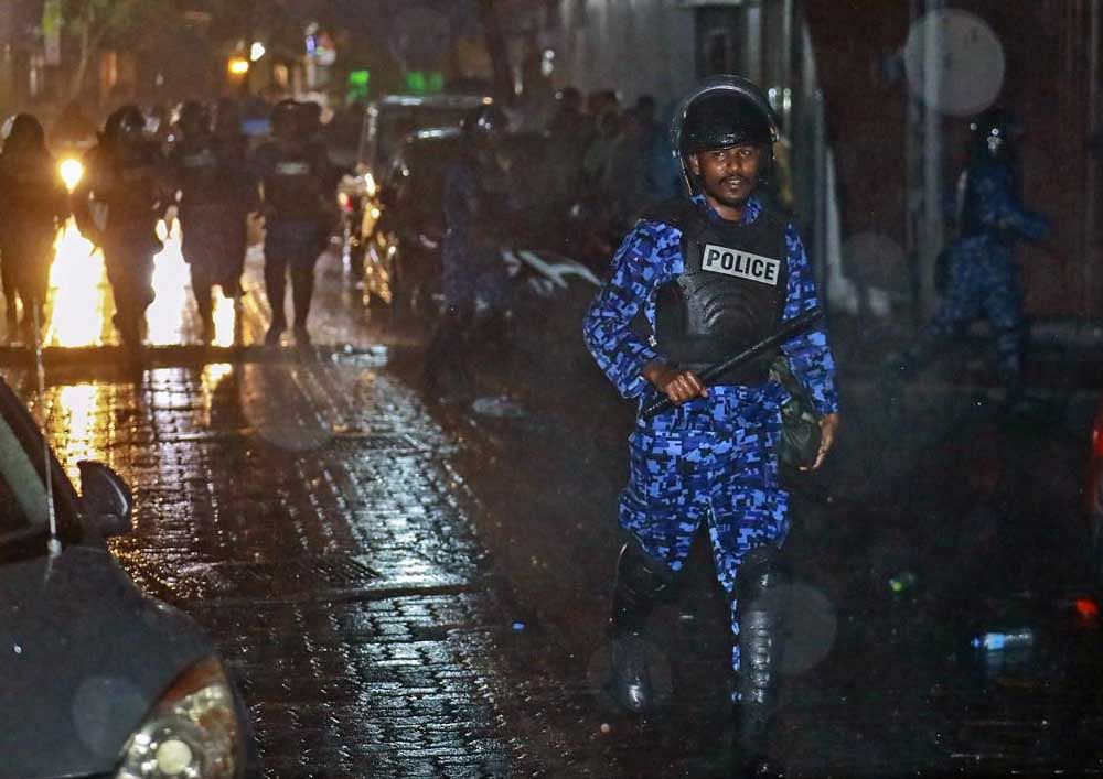 A Maldives policeman charges with baton towards protesters.