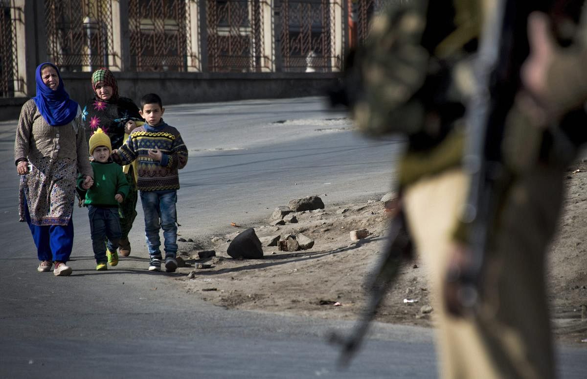 Women and children walk past a CRPF personnel standing guard during restrictions in Srinagar