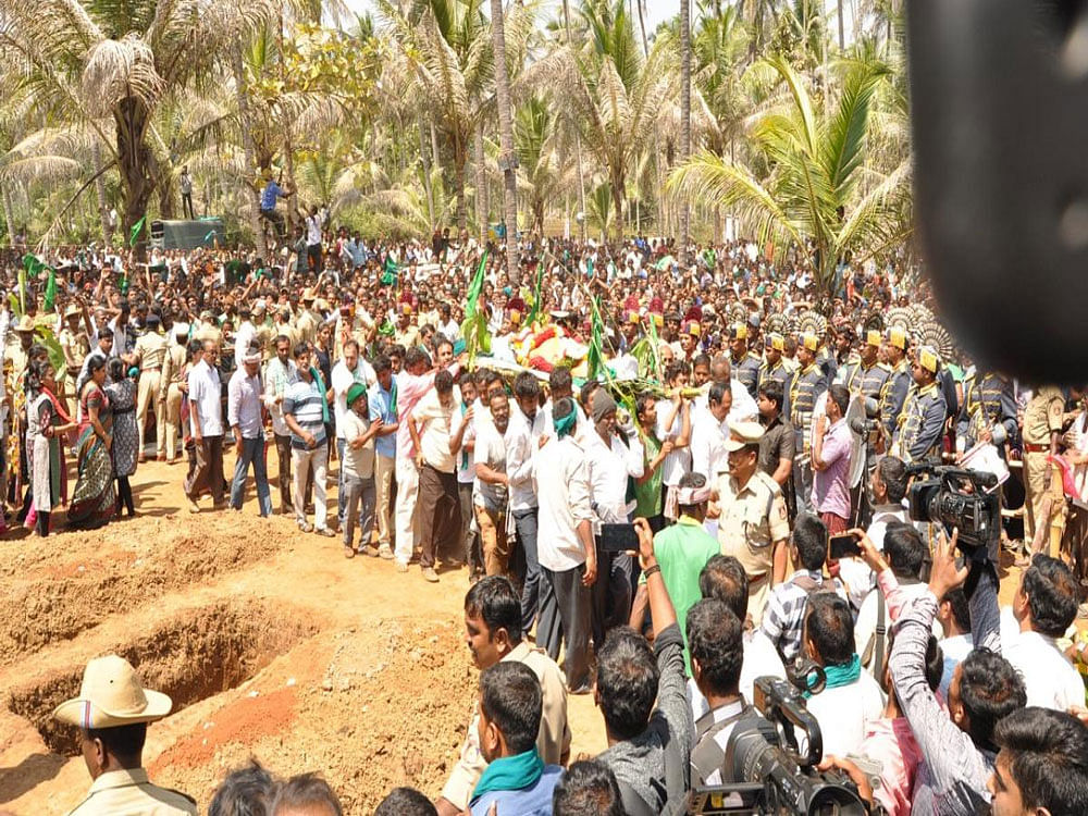 Supporters wave green flags as farmer leader K S Puttannaiah's mortal remains are brought for the funeral to his farm at Kyathanahalli, Pandavapura taluk, Mandya district, on Thursday. DH photo