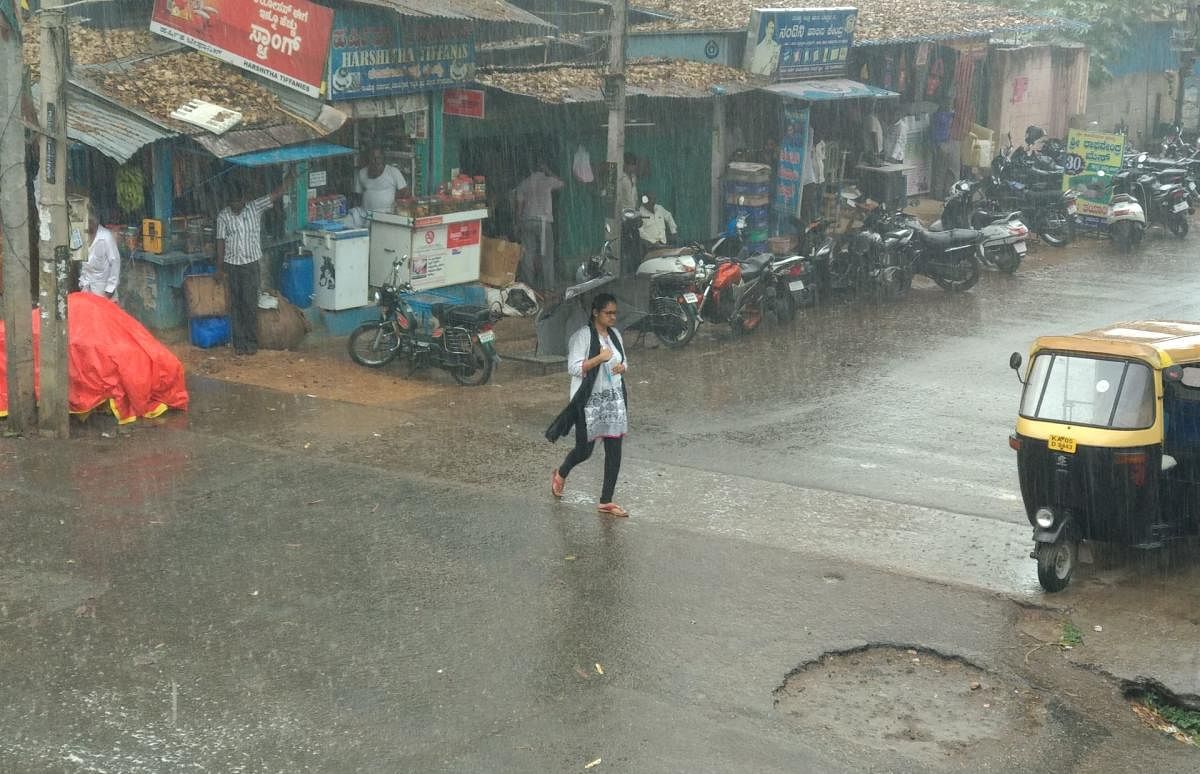 A girl protects herself from the heavy rain that lashed Mandya on Thursday noon. DH Photo