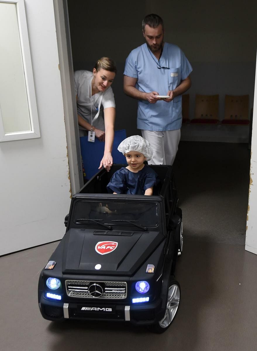 A patient drives an electric toy car on his way to the operating room. AFP
