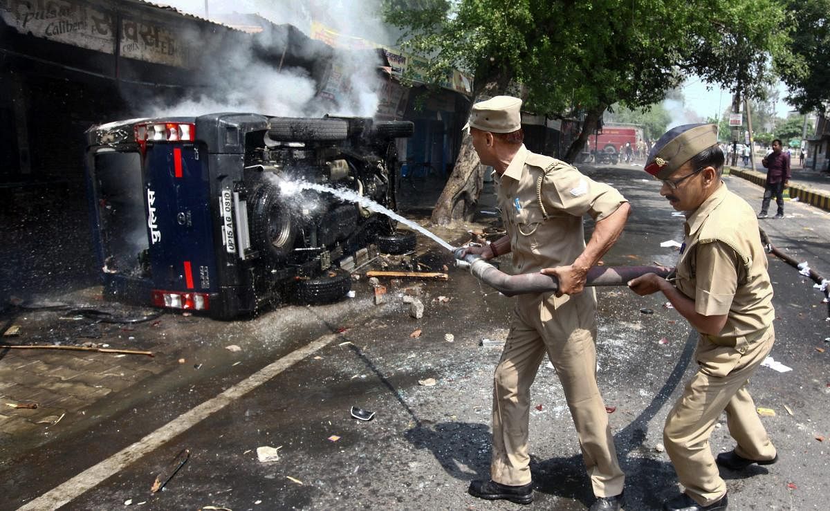 Policemen try to douse a police vehicle set on fire by protestors during 'Bharat Bandh' call given by Dalit organisations against the alleged dilution of Scheduled Castes / Scheduled Tribes act, in Meerut on Monday. PTI Photo