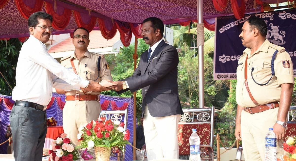 Retired SI Rajgopal distributes police welfare fund, during the Police Flag Day celebrations in Udupi. SP Lakshman Nimbargi and Additional SP Kumarachandra look on.