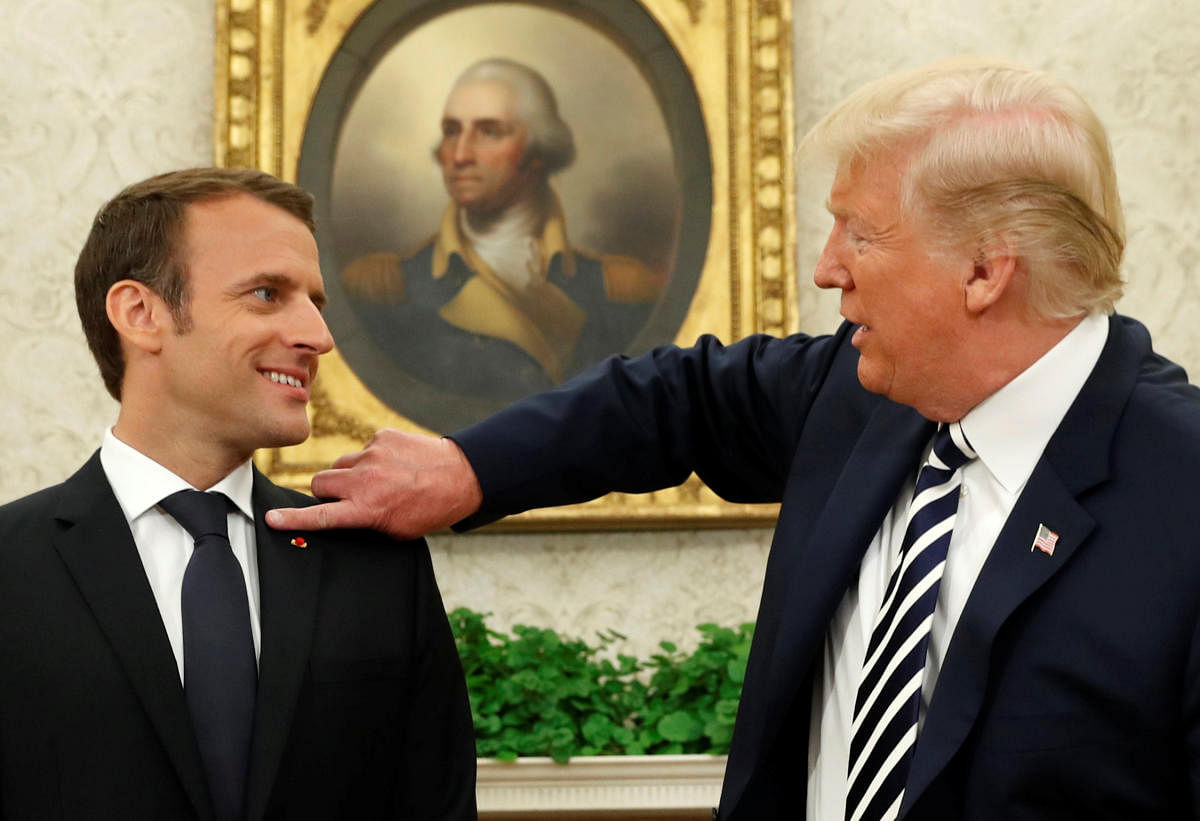 French President Emmanuel Macron (L) looks on as US President Donald Trump flicks a bit of dandruff off his jacket, in Washington on Tuesday. REUTERS
