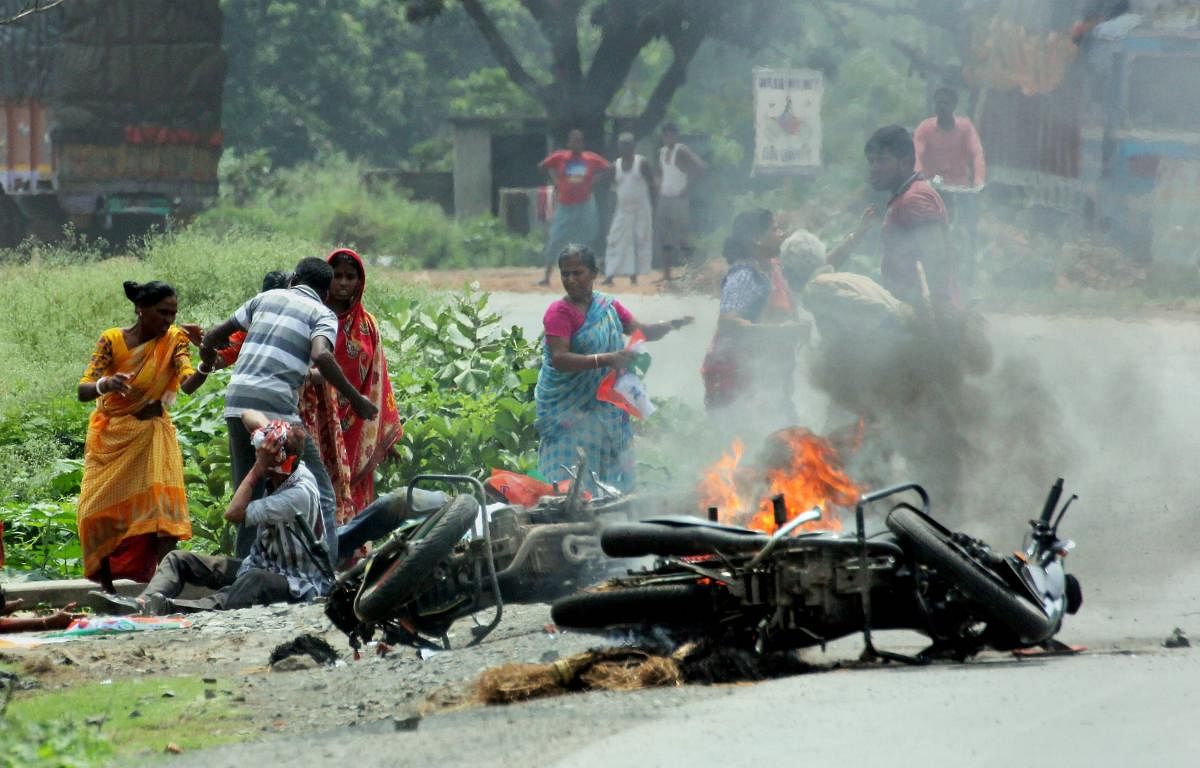 People injured in poll violence sit by the side of a road as a vehicle is set on fire by locals during panchayat polls, in Nadia district of West Bengal on Monday. PTI