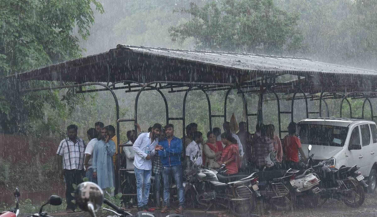 People take shelter under a two-wheeler parking stand in Dharwad after skies opened up on Wednesday evening. DH PHOTO