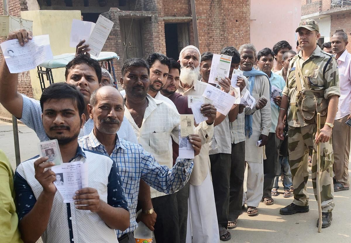 Voters show their voter identity cards as they wait in a queue to cast their votes for Noorpur Assembly bypolls, in Bijnor. PTI