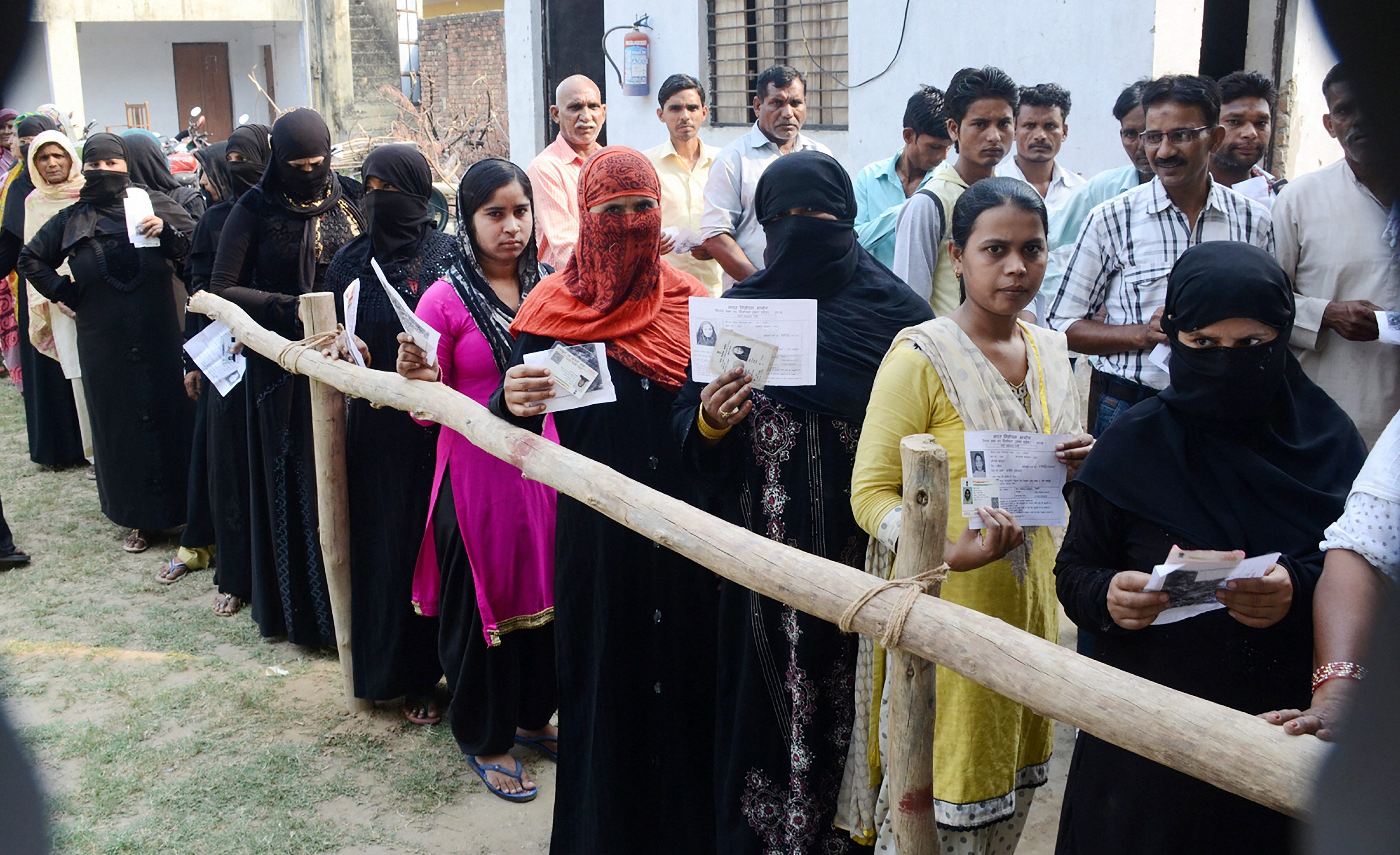 Burqa-clad women, along with other voters, show their voter identity cards as they wait to cast thier votes for Noorpur Assembly bypolls, in Bijnor, on Monday. PTI