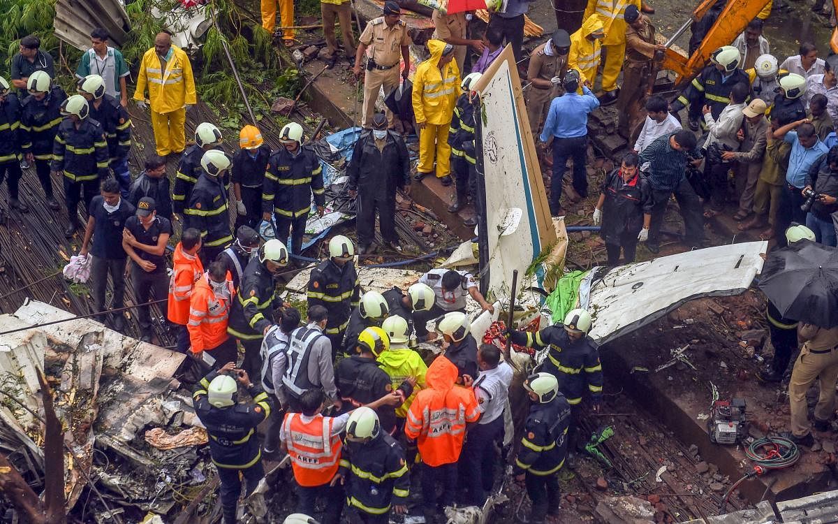Rescue personnel stand near the debris of the chartered plane that crashed in Ghatkopar's Jivdaya Lane, killing 5, in Mumbai on Thursday, June 28, 2018. PTI Photo