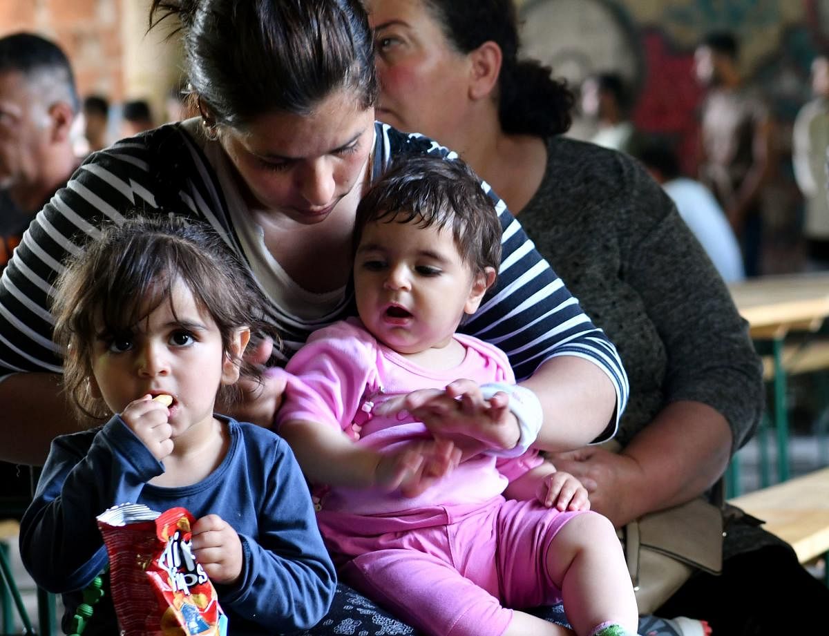 A mother sits with her children as they wait for lunch to be served at a makeshift migrant center, in the North-Western Bosnian town of Bihac, on May 31, 2018. Bosnia, one of Europe's poorest countries, is so ill-equipped to cope with a surging influx of