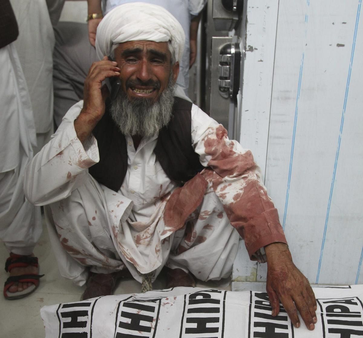 A man talks on a phone sitting next to a body of his family member killed in a bomb attack, in Quetta, Pakistan, Friday, July 13, 2018. (AP/PTI)