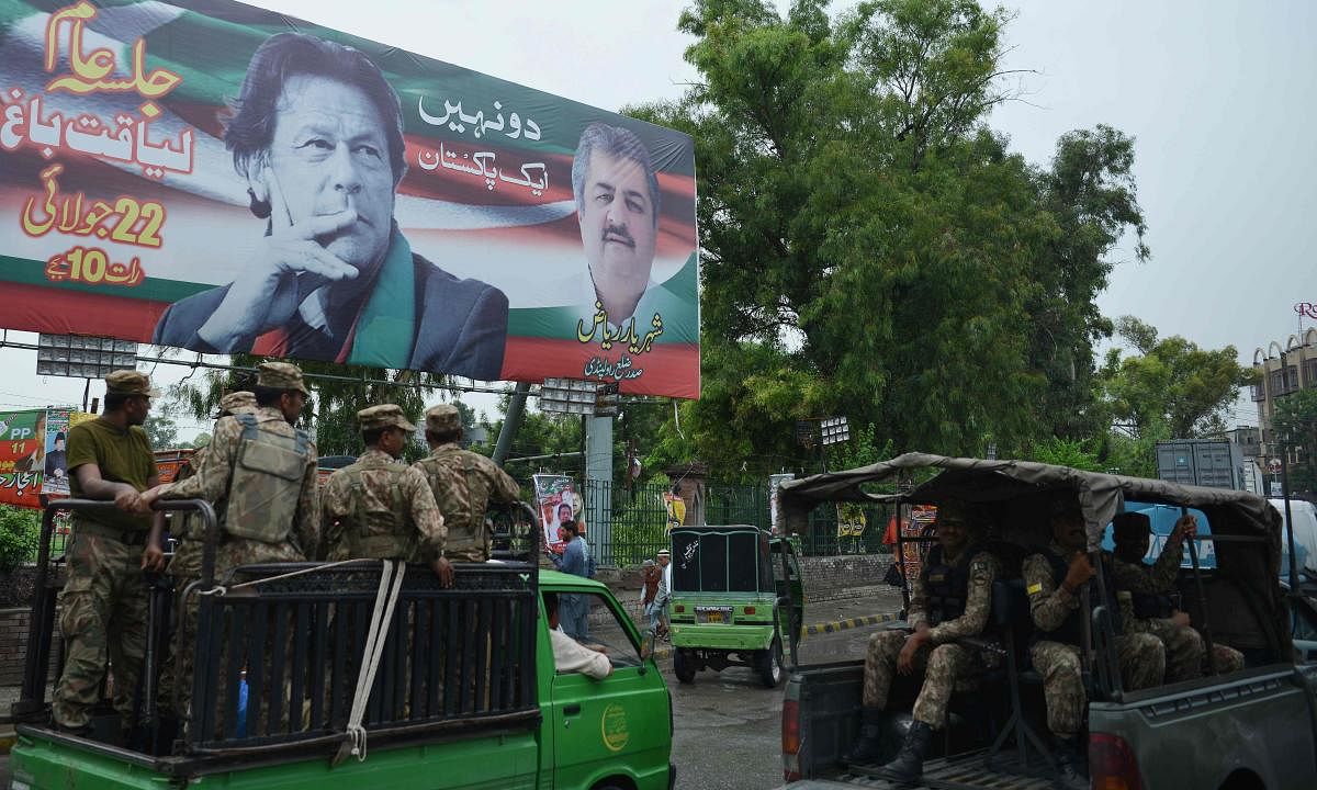 Pakistani soldiers patrol on a street beside a billboard featuring an image of Pakistani cricketer turned politician Imran Khan (top L) of the Pakistan Tehreek-e-Insaf (Movement for Justice), ahead of general election in Rawalpindi. AFP Photo
