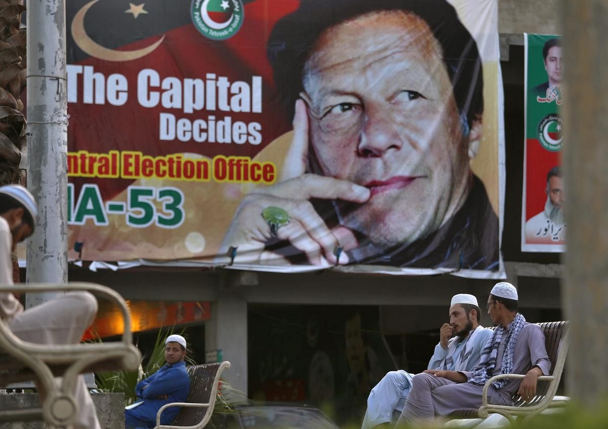 Pakistanis chat while they sit on a bench next to a big poster of Imran Khan, head of Pakistan Tehreek-e-Insaf party, at a market in Islamabad, Pakistan. AP/PTI file photo